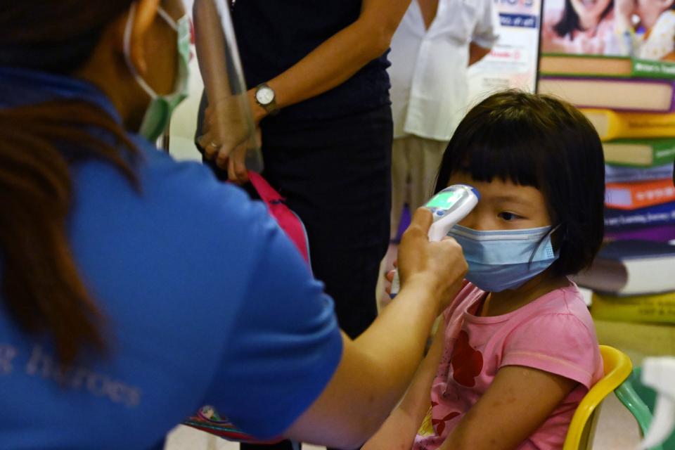 A pre-school teacher checks the temperature of a child before entering a classroom as schools reopened in Singapore on June 2, 2020, as the city state eased its partial lockdown imposed to prevent the spread of COVID-19 in Singapore. (Photo by ROSLAN RAHMAN / AFP) (Photo by ROSLAN RAHMAN/AFP via Getty Images)