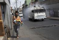 A woman runs carrying her baby as a Bolivarian National Guard water cannon sprays disinfectant as a preventive measure against the spread of the new coronavirus. in the Catia parish in Caracas, Venezuela, Tuesday, March 24, 2020. President Nicolas Maduro has ordered the entire nation to stay home under a quarantine aimed at cutting off the spread of the new virus, calling it a “drastic and necessary measure.” (AP Photo/Ariana Cubillos)