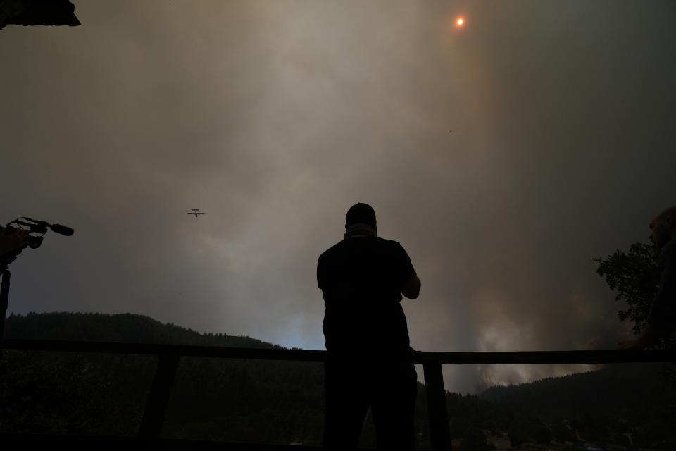 An aircraft operates over a wildfire in Gouves village on the island of Evia, about 185 kilometers (115 miles) north of Athens, Greece, Sunday, Aug. 8, 2021. Pillars of billowing smoke and ash have blocked out the sun, turning the sky orange as a massive forest fire burning for five days devours pristine forests on Greece's second largest island of Evia, triggering yet more evacuation alerts as residents appealed for greater firefighting help. (AP Photo/Petros Karadjias)