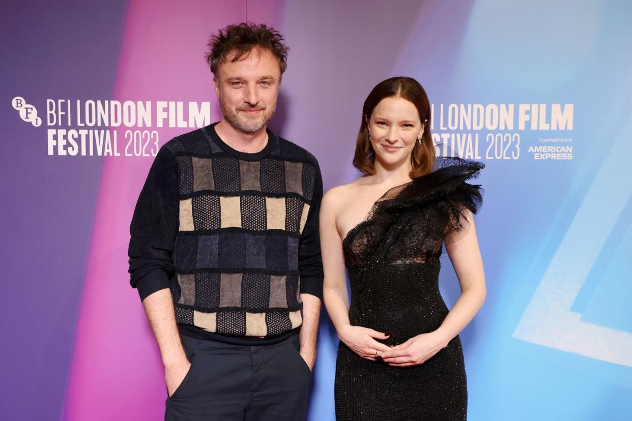 robert kokotajlo stands next to morfydd clark at london film festival, he's wearing a black jumper with squares in different colours on the front, she's wearing a one shoulder black dress embellished with crystals