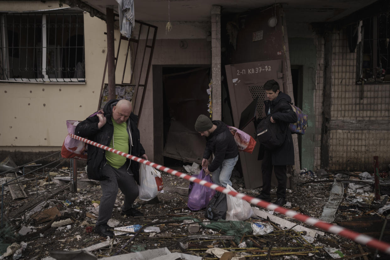 People remove their belongings from a destroyed building after it was hit by artillery shelling in Kyiv in Kyiv, Ukraine, Monday, March 14, 2022. (AP Photo/Felipe Dana)