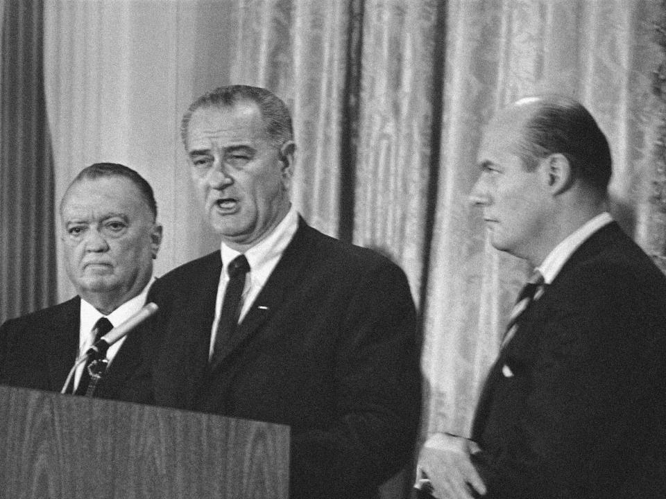 J. Edgar Hoover stands beside President Lyndon Johnson as he announces the arrest of four Ku Klux Klan members.