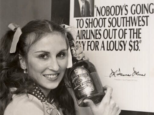 Ticket agent poses with a bottle of Chivas Regal in front of ad