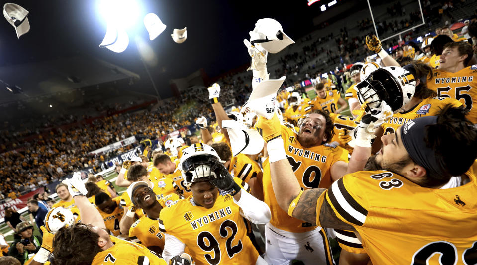 Wyoming players celebrate, grabbing championship hats being thrown their way. after defeating Toledo during the Arizona Bowl NCAA college football game Saturday, Dec. 30, 2023, in Tucson, Ariz. (Kelly Presnell/Arizona Daily Star via AP)