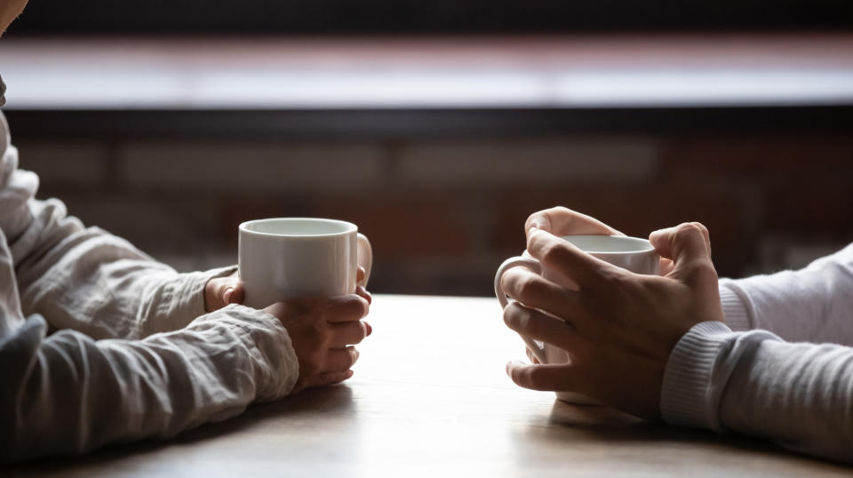 Close-up of woman and man holding cups of coffee on table