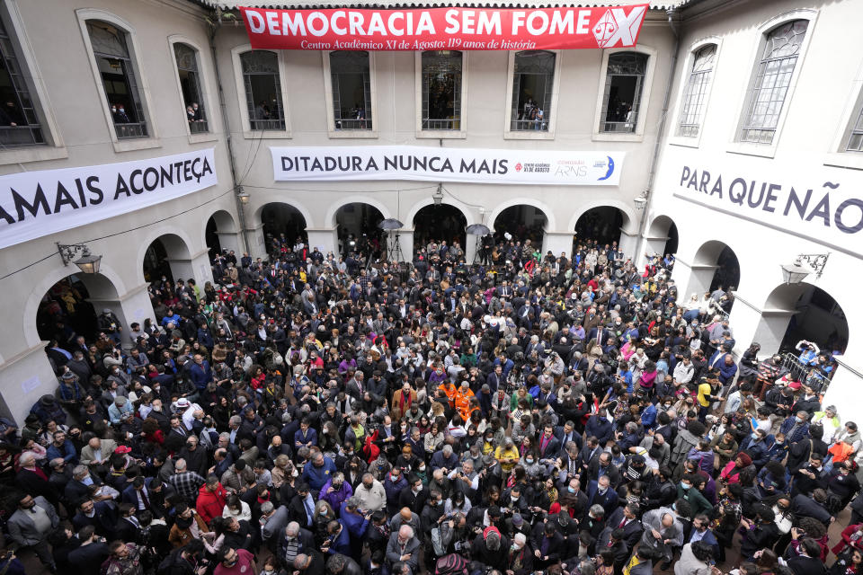 People attend the reading of one of two manifestos defending the nation's democratic institutions and electronic voting system outside the Faculty of Law at Sao Paulo University in Sao Paulo, Brazil, Thursday, Aug. 11, 2022. The two documents are inspired by the original “Letter to the Brazilians” from 1977 denouncing the brutal military dictatorship and calling for a prompt return of the rule of law. The signs read in Portuguese "Democracy without hunger," top, and "Dictator never again." (AP Photo/Andre Penner)