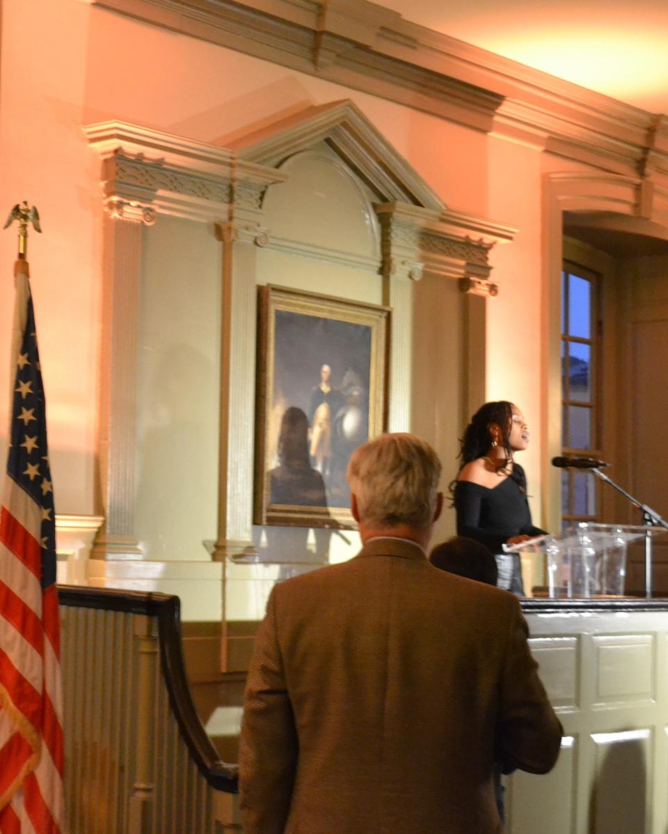 Senator Sheldon Whitehouse stands while Newport native Tavia Baker sings the national anthem at the beginning of the League of Women Voters of Newport County's Votes not Violence candlelight vigil commemorating the anniversary of the January 6, 2021, storming of the US Capitol.