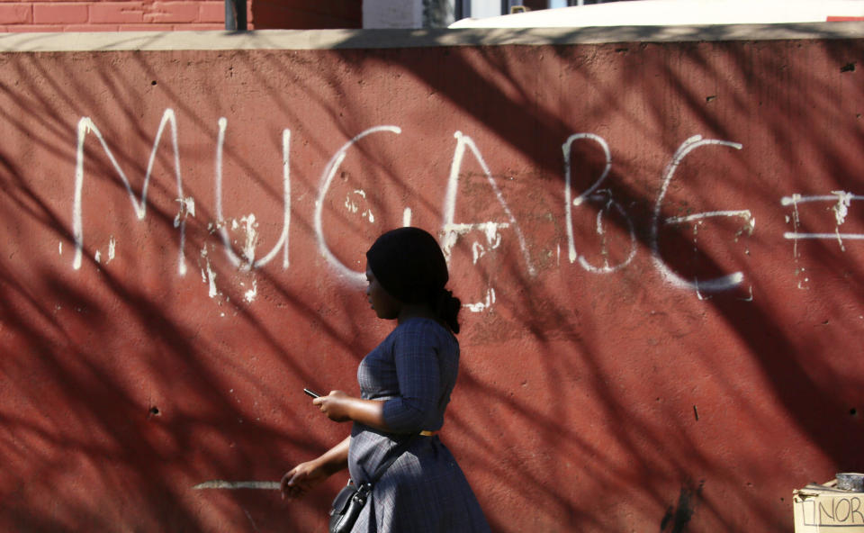 A woman walks past a graffiti sign in Harare, Friday, Sept. 6, 2019. Robert Mugabe, the former leader of Zimbabwe forced to resign in 2017 after a 37-year rule whose early promise was eroded by economic turmoil, disputed elections and human rights violations, has died. He was 95. (AP Photo/Tsvangirayi Mukwazhi)