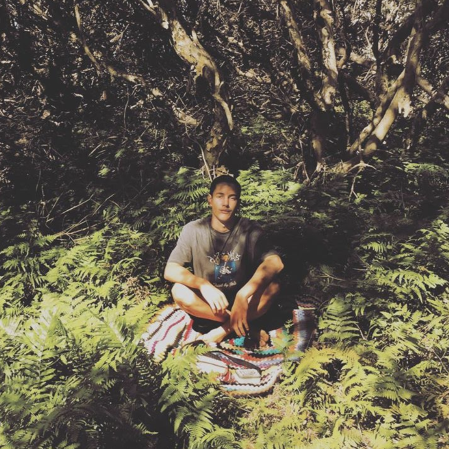 Mani Hart-Deville is pictured sitting in a rainforest. 