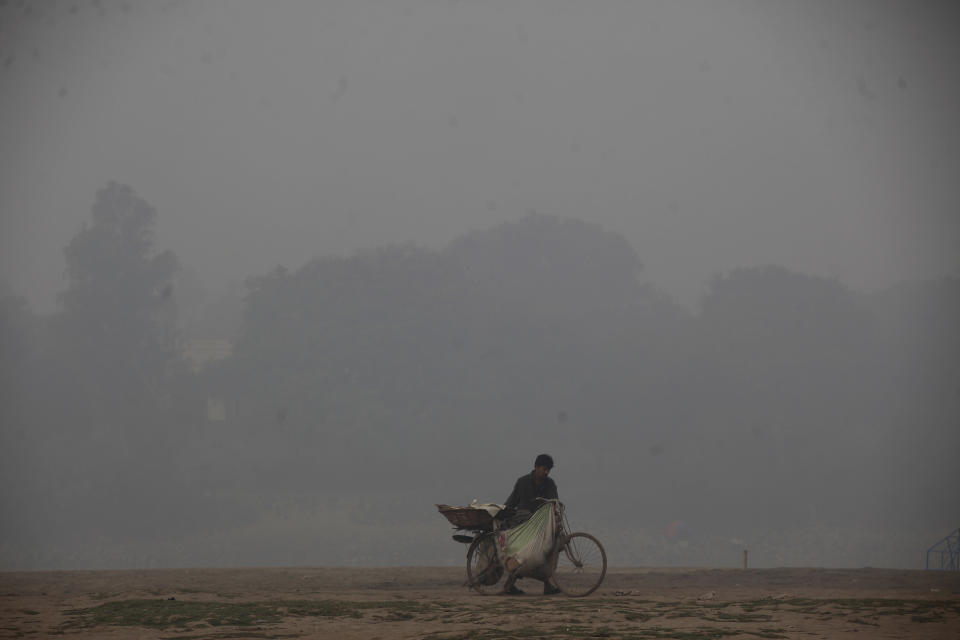 A cyclist pushes his laden bike through smog, in Lahore, Pakistan, Thursday, Nov. 21, 2019. Amnesty International issues "Urgent Action" saying every person in Lahore at risk. Heavy smog has enveloped many cities of Punjab province, causing highway accidents and respiratory problems, and forcing many residents to stay home. (AP Photo/K.M. Chaudary)