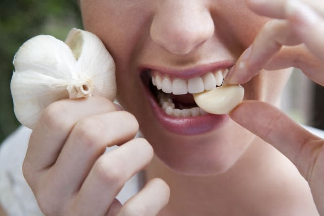 close up of woman biting into a garlic clove