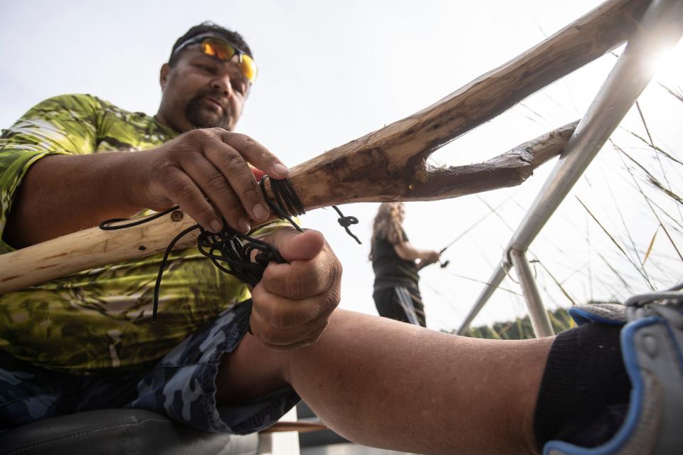 Bay Mills Community College farm technician Dennis Carrick ties rope around a section of a handmade push-pull pole to be used to navigate a canoe through the tall grass where manoomin "wild rice" grows on a section of the Au Sable River in Oscoda on Sept. 16, 2023, to be harvested. Lightweight wood is used for the handle to avoid fatigue and the bottom y-shaped sections is made from a hardwood to avoid splitting. The shape helps avoid pulling the roots out of the ground and killing the plants while a person walks the canoe along the water and another knocks the grains into the boat.