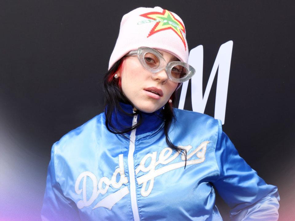 Billie Eilish staring at camera wearing a Dodgers jacket and pink beanie