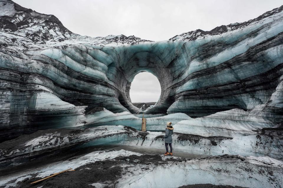 Katla glacier formation with a circular hole in the center of it with a woman standing in front of it