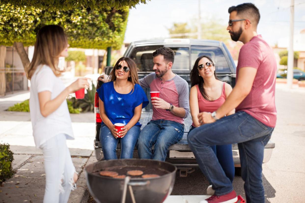Group of good looking young friends having a good time on tailgate while drinking beer and grilling burgers