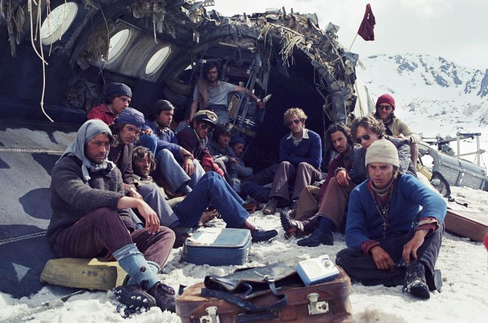 a scene from the movie society of the snow with survivors sitting near a wrecked airplane