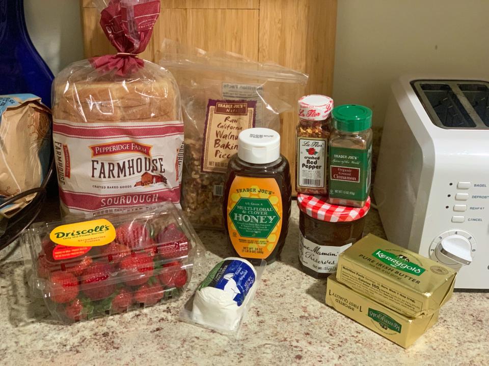 a group of groceries including strawberries, goat cheese, bread, honey, butter, jam, etc.