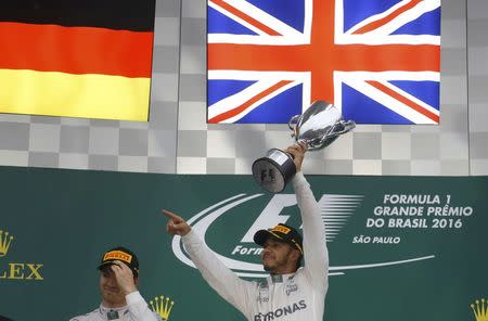 Formula One - F1 - Brazilian Grand Prix - Circuit of Interlagos, Sao Paulo, Brazil - 13/11/2016 - Mercedes' Lewis Hamilton of Britain raises his trophy during the victory ceremony after winning the race as second placed finisher and teammate Nico Rosberg of Germany (L) looks on. REUTERS/Nacho Doce