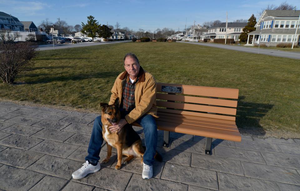 Falmouth Select Board member Doug Brown, with his dog Daisy, sits on a bench at the park at Worcester Court across the street from Falmouth Heights Beach. Brown opposes the proposed use of a horizontal directional drill in the park and underground cable below the beach that could provide infrastructure for the offshore wind farm developer, Mayflower Wind.