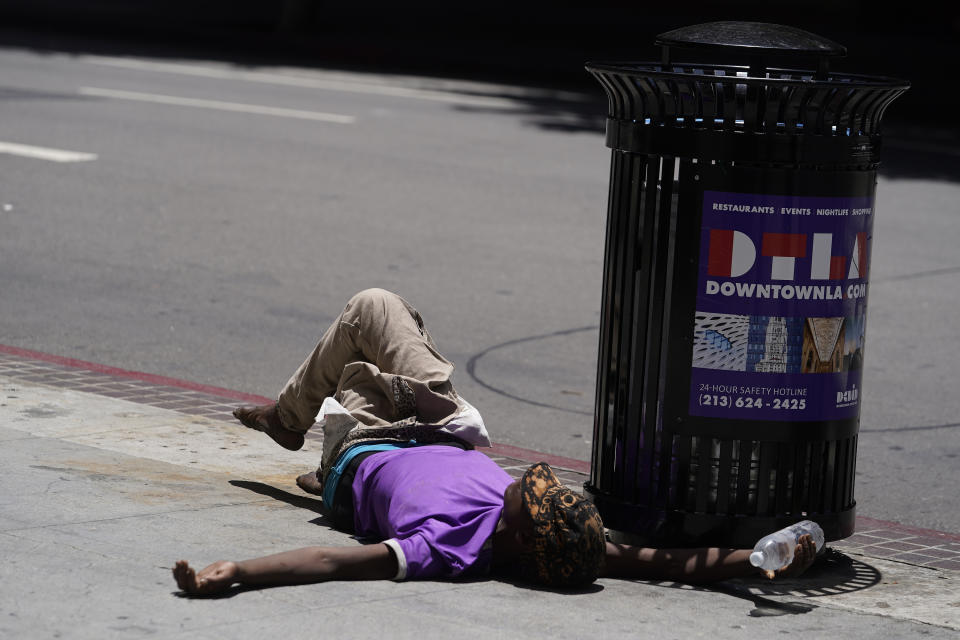 Un indigente yace sobre la acera con una botella de agua en la mano, el domingo 2 de julio de 2023, en el centro de Los Ángeles. (AP Foto/Damian Dovarganes)