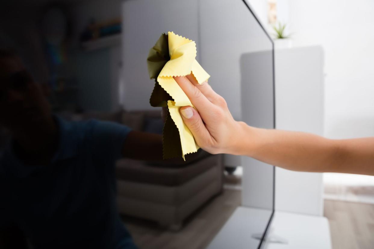 Close-up Of Woman Using Cloth To Clean The Television At Home