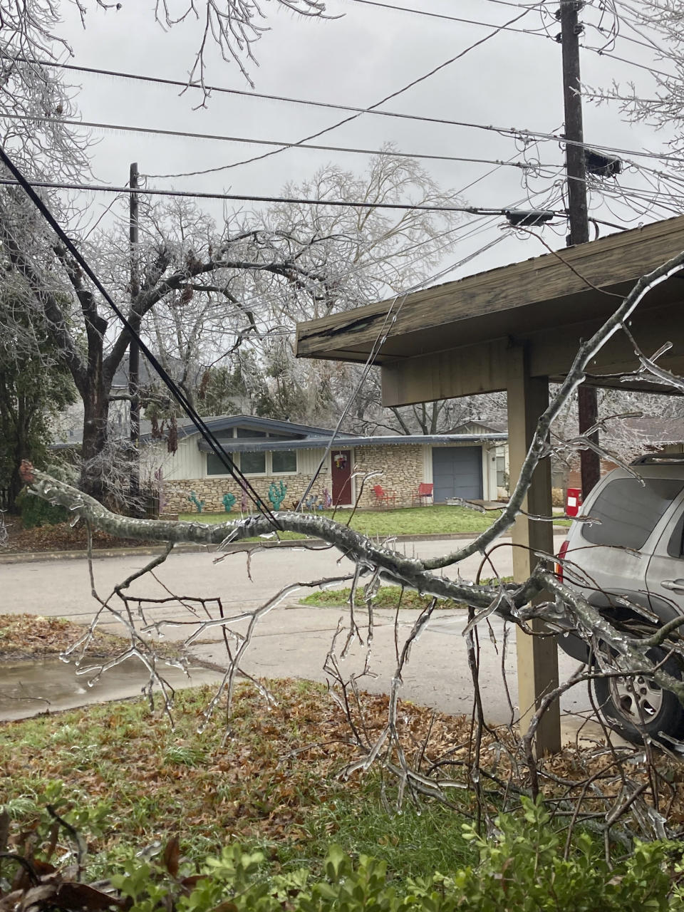 A downed branch from an ice-laden pecan tree dangles on cable lines outside of a house after a storm hit the region, Thursday, Feb. 2, 2023, in Austin, Texas. Even as temperatures finally pushed above freezing in Austin — and were expected to climb past 50 degrees (10 Celsius) on Friday — the relief will be just in time for an Arctic front to drop from Canada and threaten northern states. (Andrea Ball/Houston Chronicle via AP)