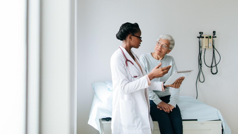 A young female doctor explaining to a senior female patient using a digital tablet in a hospital room.