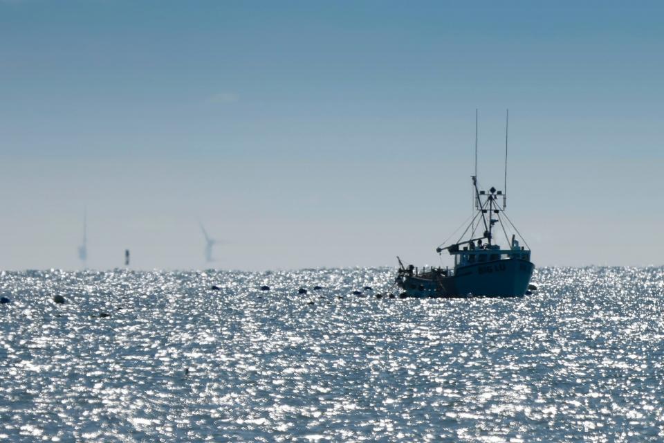 A boat is seen fishing in Buzzards Bay as seen from East Beach in Westport on a clear day. In the far distance the offshore wind turbines can be seen being constructed.