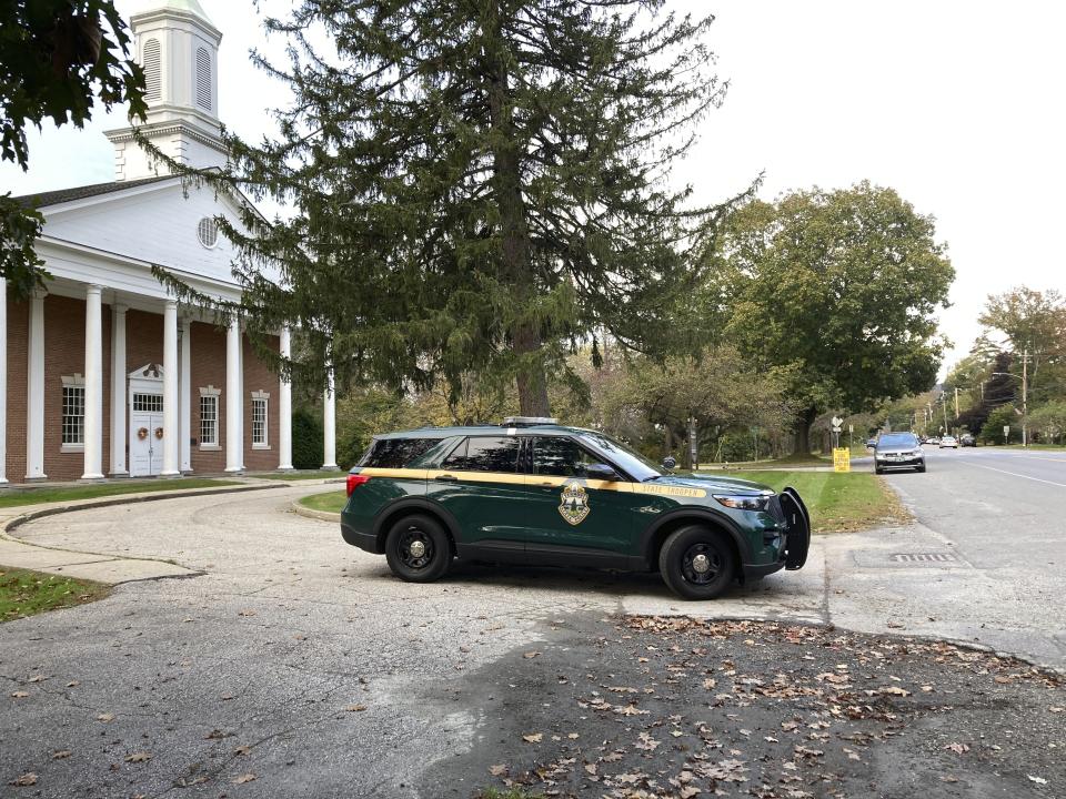 A Vermont State Police trooper is parked on Main Street in front of a church near the Vermont State University Castleton Campus on Tuesday, Oct. 10, 2023 in Castleton, Vt.. Police were searching for a suspect who shot and killed a retired dean on a nearby rail trail last week. (AP Photo/Lisa Rathke)