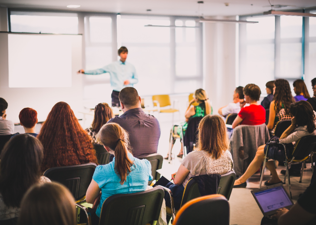 A person stands at the front of a classroom of adult students.