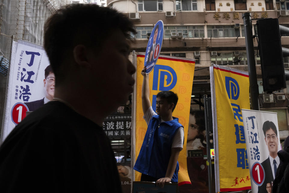 A pedestrian walks past campaigners promoting candidates during the District Council elections in Hong Kong, Sunday, Dec. 10, 2023. Residents went to the polls on Sunday in Hong Kong's first district council elections since an electoral overhaul was implemented under Beijing's guidance of “patriots” administering the city, effectively shutting out all pro-democracy candidates. (AP Photo/Louise Delmotte)