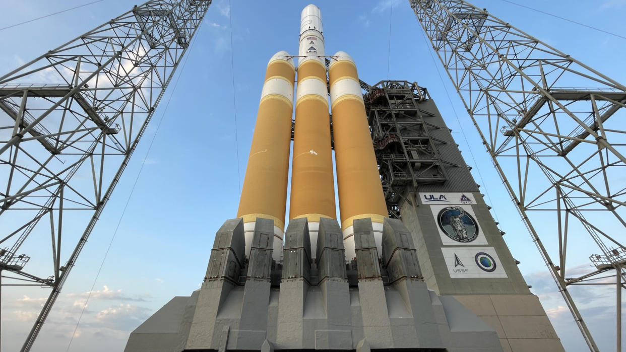  A white and orange rocket stands upright on a launch pad. 