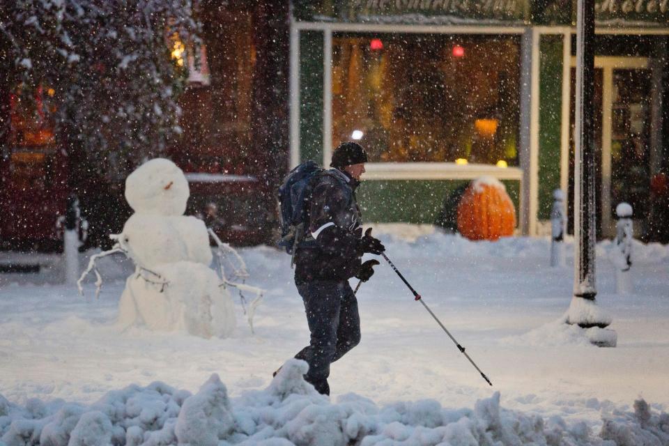 A man uses ski poles to help him walk past a snowman in downtown Bangor Sunday, November 2, 2014, after an early season snowstorm slapped parts of Maine including Bangor with multiple inches of snow Sunday, November 2, 2014.