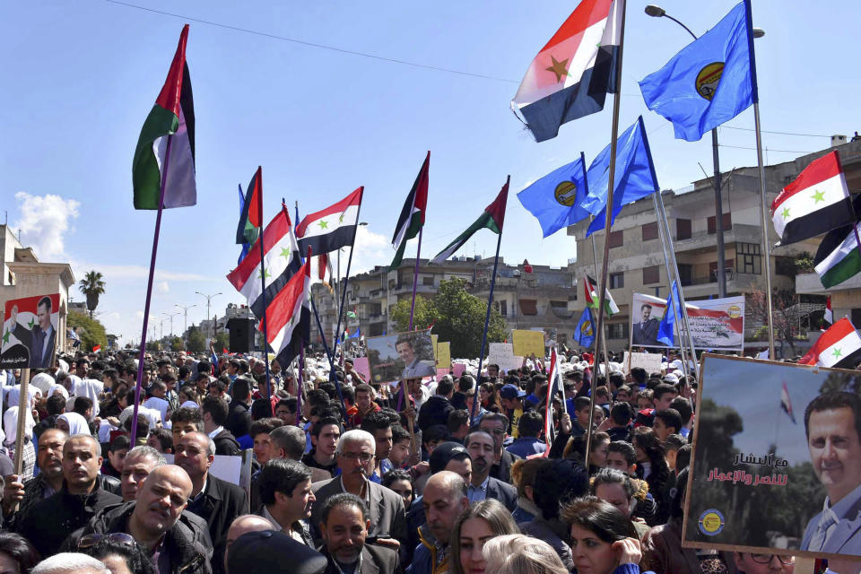In this photo released by the Syrian official news agency SANA, Syrians hold national flags and portraits of Syrian President President Bashar Assad during a protest against President Donald Trump's move to recognize Israeli sovereignty over the Israeli occupied Golan Heights, in Homs, Syria, Tuesday, March 26, 2019. Syria's state news agency says thousands of Syrians have held gatherings in the streets of different cities to protest Trump's signing of a declaration reversing US policy on the Golan Heights. (SANA via AP)