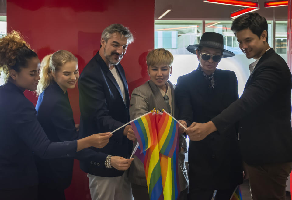 A diverse group of six people touching their Pride flags together