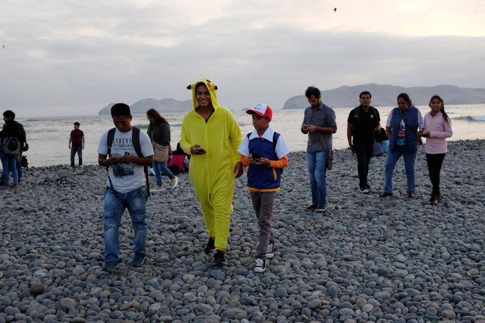 People walk with their mobile phones as some play Pokemon GO at La Punta beach in Callao, Peru: REUTERS/Mariana Bazo