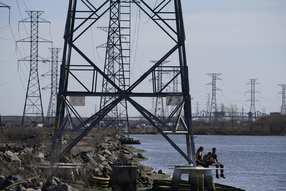 People sit at the base of a transmission tower in North Arlington, N.J., Tuesday, April 6, 2021. President Joe Biden is setting about convincing America it needs his $2.3 trillion infrastructure plan, deputizing a five-member "jobs Cabinet" to help in the effort. But the enormity of his task is clear after Senate Minority Leader Mitch McConnell's vowed to oppose the plan "every step of the way." (AP Photo/Seth Wenig)