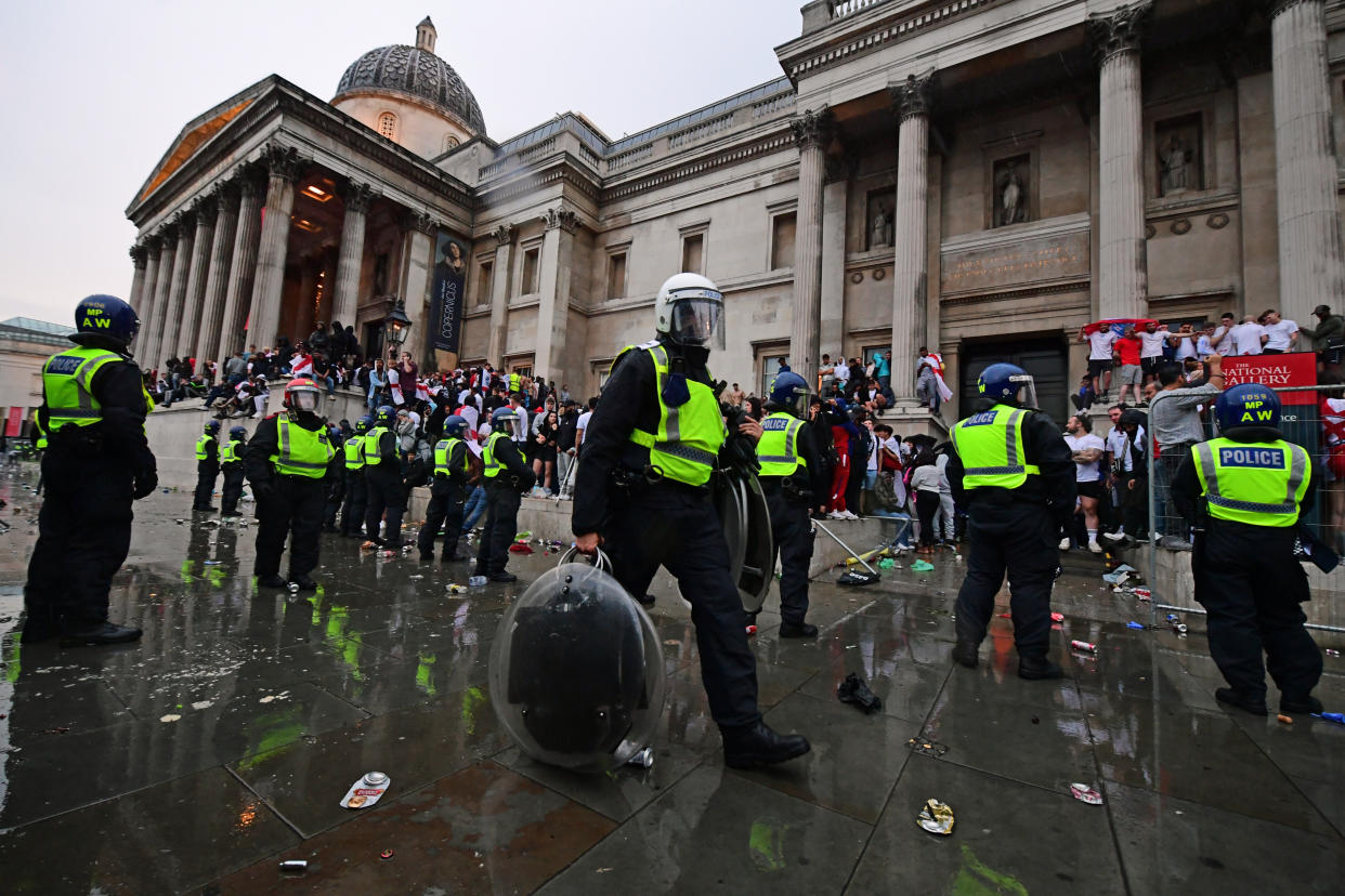 A police officer carries riot shields as colleagues observe England fans on the steps of the National Gallery, in Trafalgar Square, London during the UEFA Euro 2020 Final between Italy and England. Picture date: Sunday July 11, 2021.