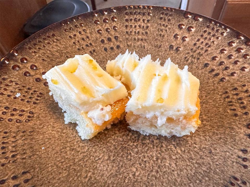 Three small pieces of a lemon cake with a light-yellow frosting on a brown plate