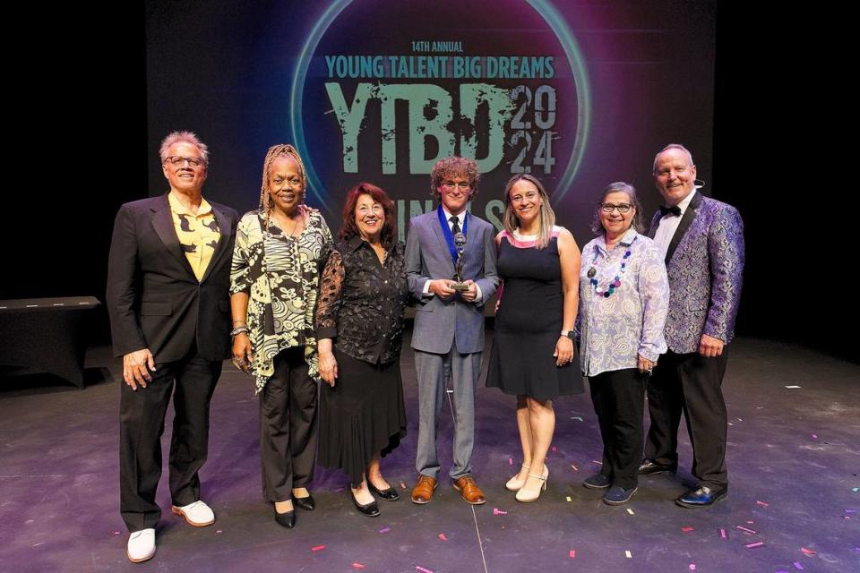 Young Talent Big Dreams 2024 original composition winner and overall grand prize champion Gerry Ibarra, 16, celebrates his victories in a group photo from the Actors’ Playhouse stage on May 11, 2024. From left to right: YTBD finals judges Howard Cohen and Shamele Jenkins, Actors’ Playhouse Executive Producing Director Barbara Stein, Gerry Ibarra, The Children’s Trust’s Director of Communications Ximena Nunez, YTBD finals judge Ruby Romero-Issaev and Actors’ Playhouse Theatre for Young Audiences Director Earl Maulding.