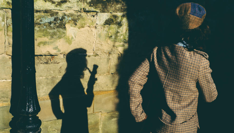 Pretty elegant young woman, Sherlock Holmes style, smoking pipe and projecting shadow of herself on wall, in a mysterious attitude.