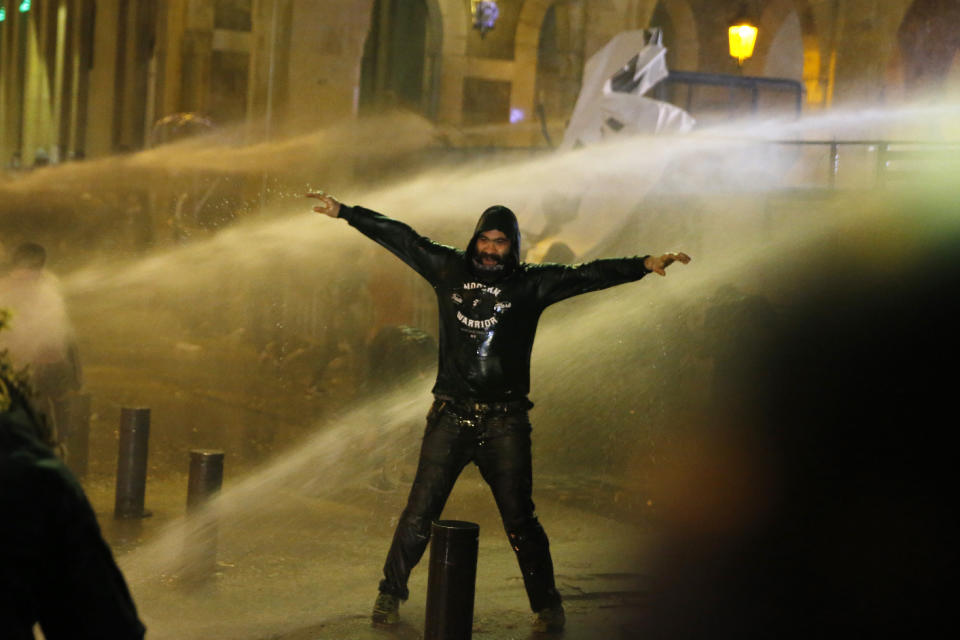 Anti-government protesters are sprayed by a water cannon as they clash with the riot police during ongoing protests in Beirut, Lebanon, Wednesday, Jan. 22, 2020. Lebanon's new government has held its first meeting a day after it was formed following a three-month political vacuum. (AP Photo/Bilal Hussein)