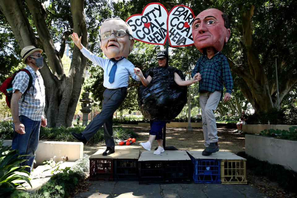 A man and a woman stand next to two people with oversized paper mache puppet heads on top of their heads. (Source: Getty)