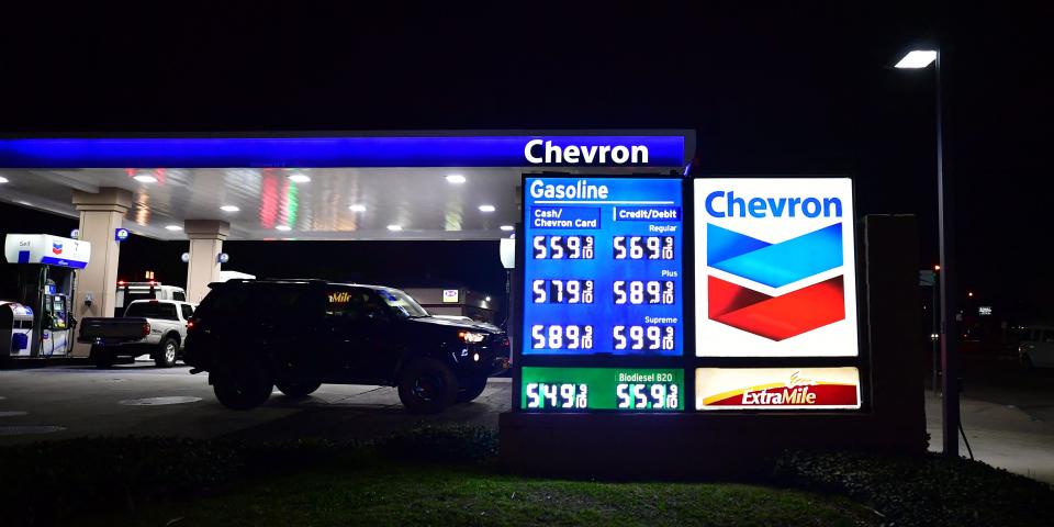 A sign at a Chevron gas station at night displays high prices.