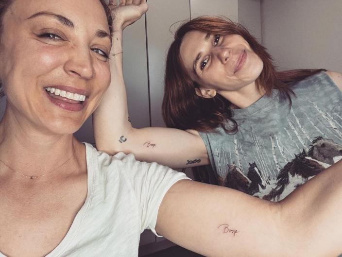 Actors Kaley Cuoco and Zosia Mamet showing off matching tattoos of the word &quot;boop&quot; on their biceps in a selfie.