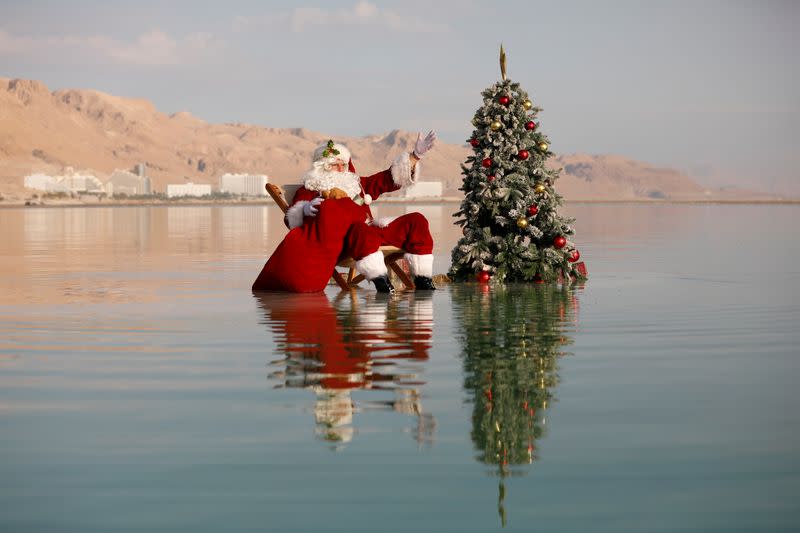 Issa Kassissieh, wearing a Santa Claus costume, gestures as he poses for a picture while sitting next to a Christmas tree on a salt formation in the Dead Sea, near Ein Bokeq