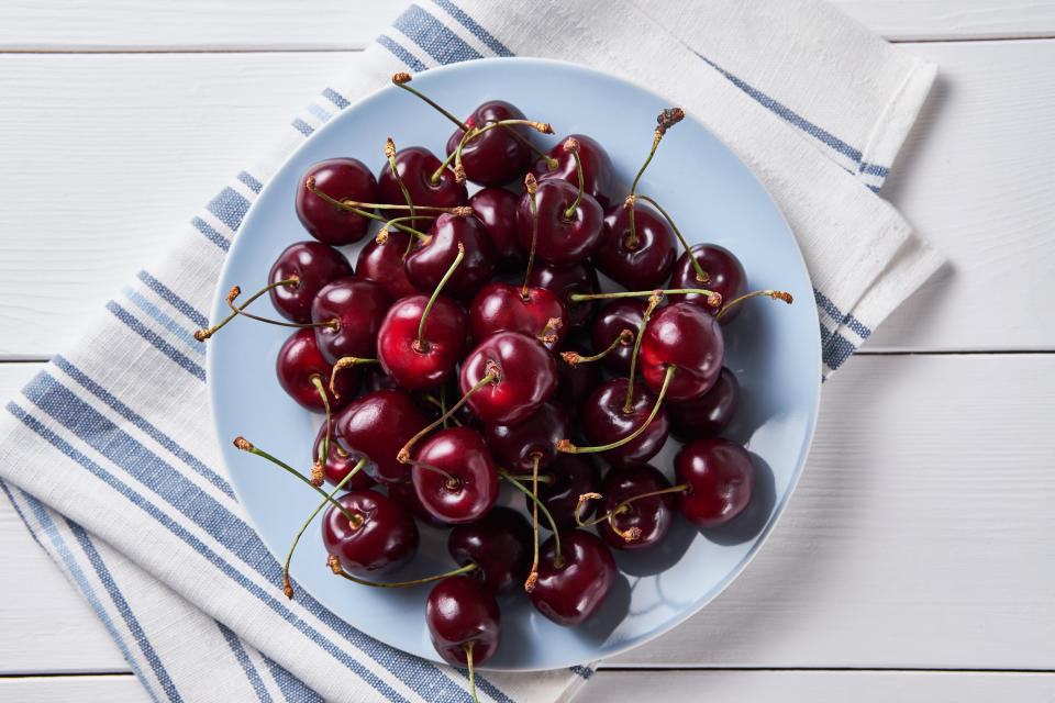 A bunch of deep red cherries on a blue plate, placed on a white and blue linen cloth on a white table background