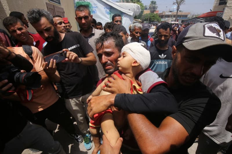 A Palestinian man carries a little kid to receive medical treatment at Al-Aqsa Martyrs Hospital following simultaneous Israeli attacks on Nuseirat Refugee Camp, al-Bureij Refugee Camp and al-Maghazi Refugee Camp. Israeli special forces rescued four hostages in broad daylight on Saturday from the Nuseirat refugee district in the centre of the Gaza Strip after 246 days in captivity, the army said. Omar Naaman/dpa