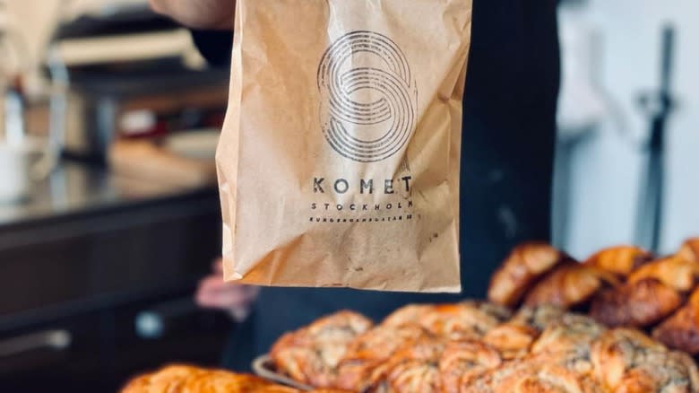 person holding to go brown bag in bakery