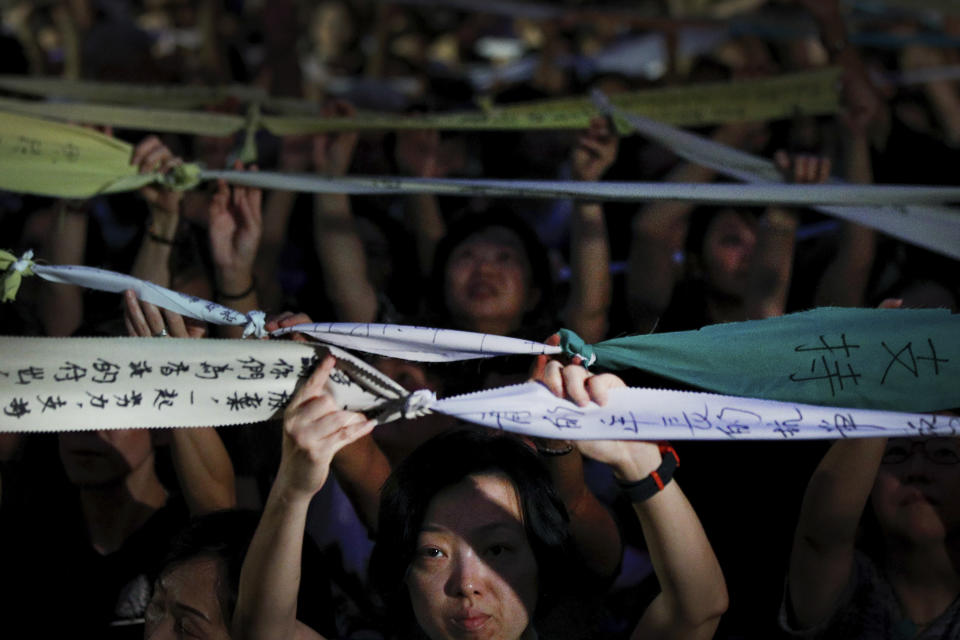 A beam of spotlights is cast on a woman face as she and attendees hold up tied message written banners during a rally by mothers in support of student protesters in Hong Kong on Friday, July 5, 2019. Hong Kong's societal divide showed no sign of closing Friday as students rebuffed an offer from city leader Carrie Lam to meet and a few thousand mothers rallied in support of young protesters who left a trail of destruction in the legislature's building at the start of the week. (AP Photo/Andy Wong)